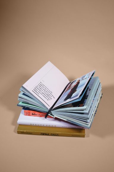 A stack of colorful books and magazines, some open, on a beige background.