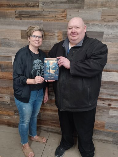 Two people, a man and a woman, holding a book together against a wooden background.