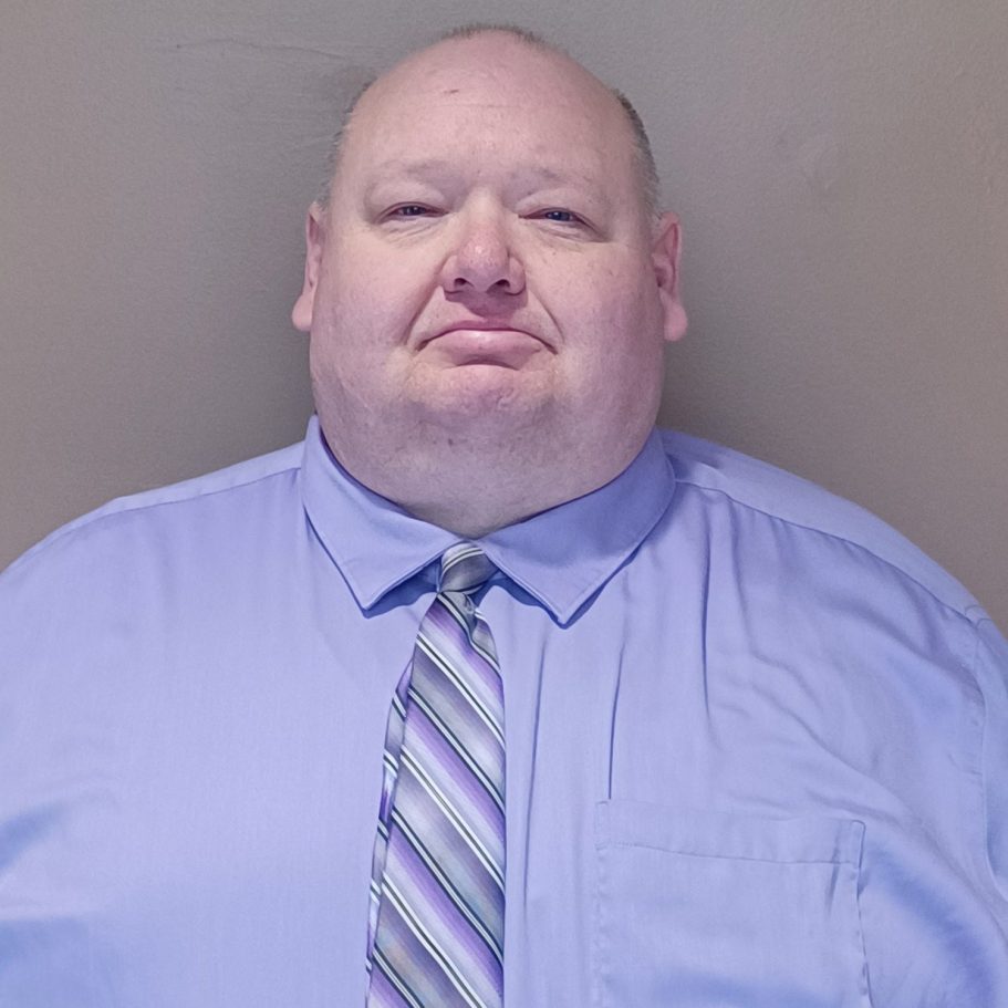 A man with a bald head and a blue dress shirt, wearing a striped tie.
