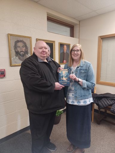 Two people, a man and a woman, stand together smiling while holding a book.