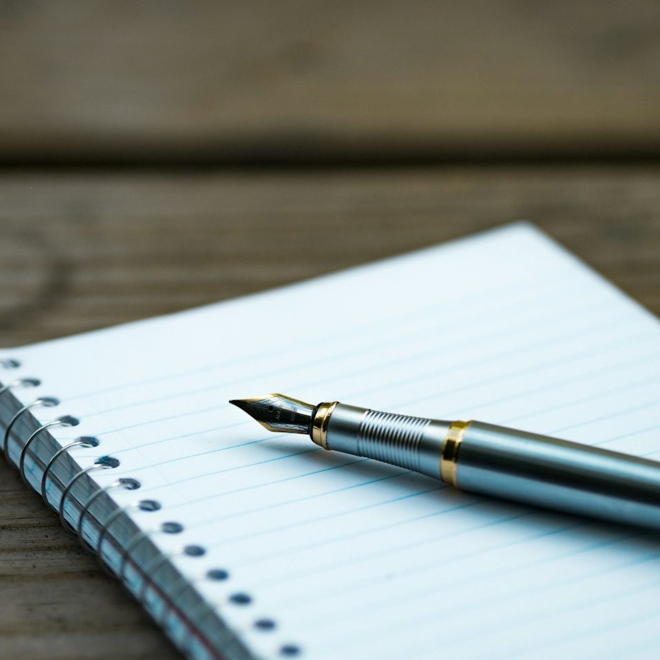 A fountain pen resting on a blank notepad with a wooden surface.